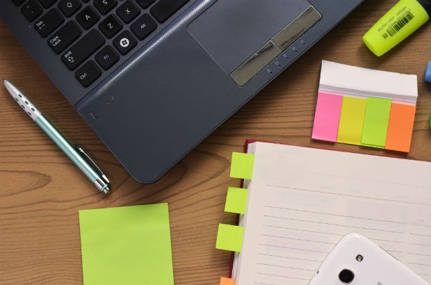 Laptop, Post-It notes and a blank notepad on a table.