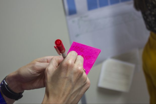 woman holding a pink post it note and writing on it with a pen
