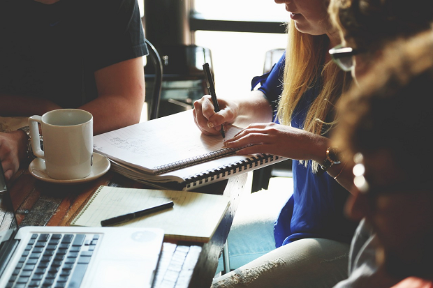 Four individuals sitting a desk having a disucssion and making notes on a notepad