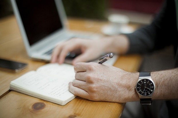 Gentleman sat at a desk writing notes in a notepad 