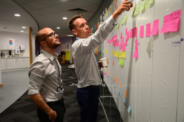 Product Manager, Andy, and another colleague having a meeting by the release wall