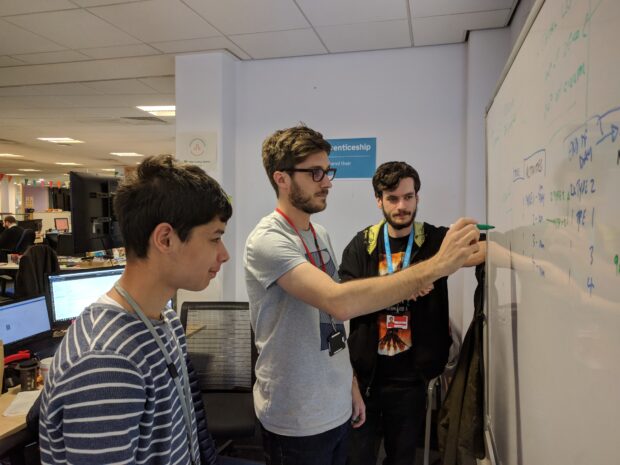 Arun, and two other apprenticeship service colleagues, standing next to a white board having a meeting 