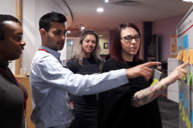 Four user research colleagues having a discussion at a meeting wall, using post-it notes to write ideas down