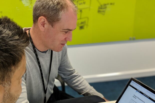 Paul Kelman, Product Owner, looking at a computer screen with a colleague 